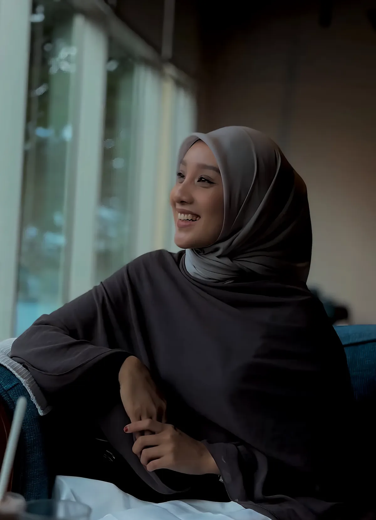 Aini Junaidi laughing at a cafe window in a grey hijab